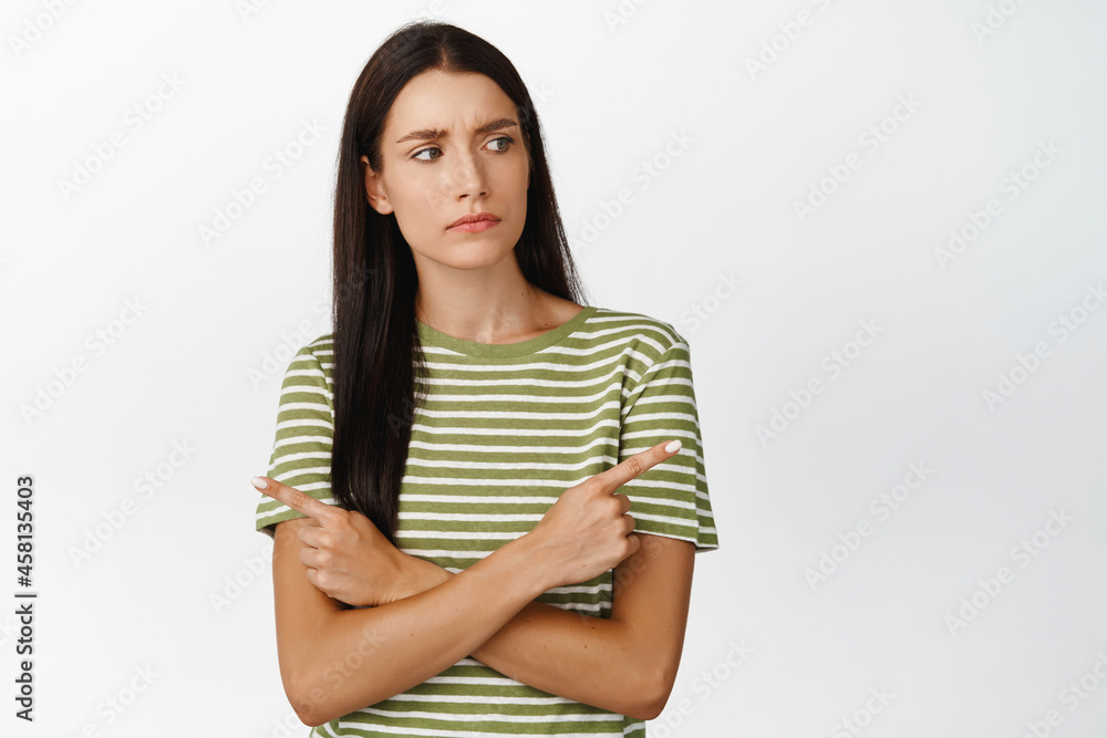 Indecisive brunette woman looking with doubt, pointing sideways, making decision with troubled face, standing over white background Indecisive brunette woman looking with doubt, pointing sideways, making decision with troubled face, standing over white background