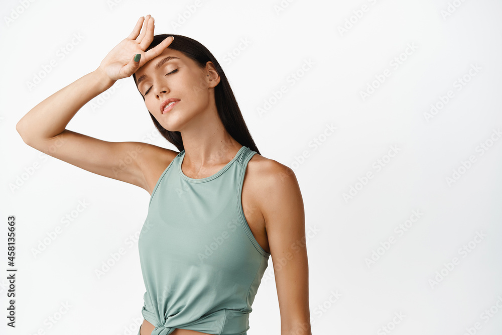 Portrait of beautiful young sportswoman wipe sweat off forehead and close eyes with pleased face, satisfied after productive workout training session, white background Portrait of beautiful young sportswoman wipe sweat off forehead and close eyes with pleased face, satisfied after productive workout training session, white background