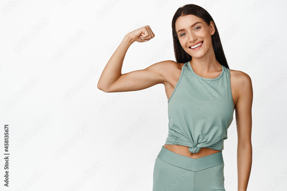 Smiling brunette fitness girl showing muscles on arm, flexing