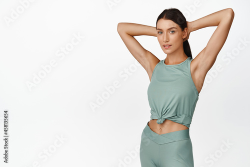 Young female athlete comb her hair, prepare for workout, doing fitness exercises, standing in activewear against white background