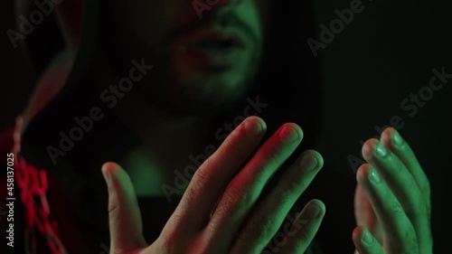 Evil exorcist reading spell close-up. Wicked shaman magician wearing robe and chains standing in darkness, making ritual, scary wizard using witchcraft, black magic. Halloween concept. 