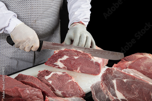 Close up of minced meat pieces and butcher's male hands in special gloves cutting with knife. Meat pork or beef on the butcher's table. Worker in white uniform and special steel apron.