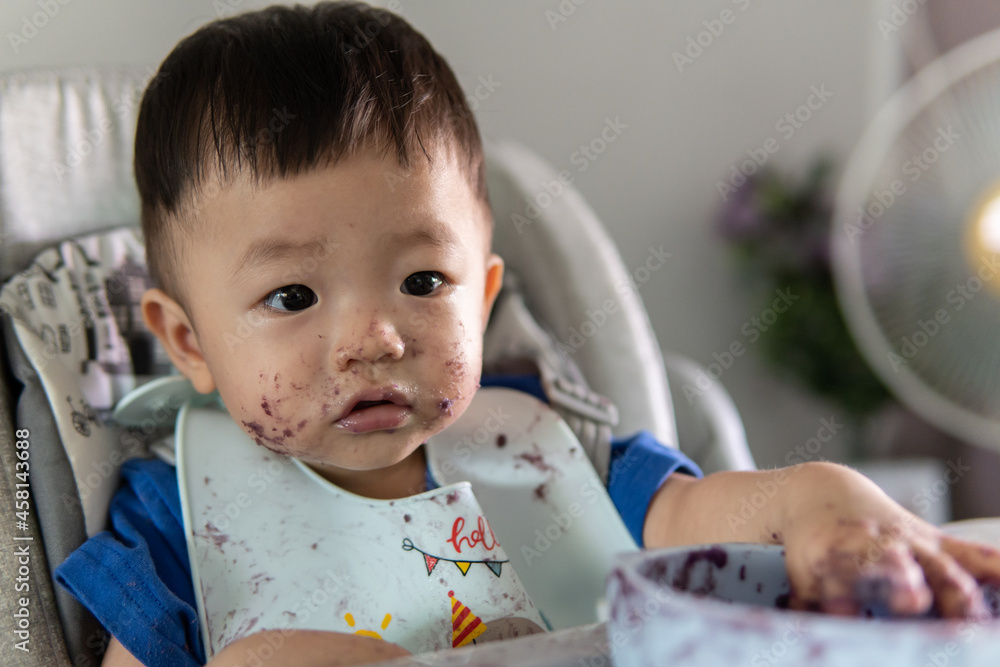 adorable and cute happy Asian Chinese baby boy siting on baby chair enjoying meal with dirty face adorable and cute happy Asian Chinese baby boy siting on baby chair enjoying meal with dirty face