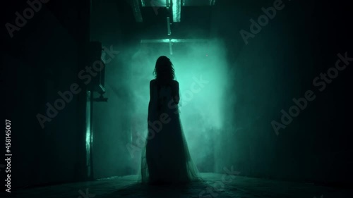 Dead walking zombie woman in dark corridor and mist close-up. Creepy bride wearing wedding dress with veil. Deceased fiancee returned to life. Horrible klip on halloween. Haunted house.  photo
