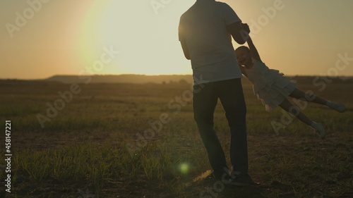 Happy father circling a small child at sunset, silhouette of dad and daughter, happy family, childhood dream, want to learn to fly, play outdoors, cheerful fantasy to climb up to the sky, day off