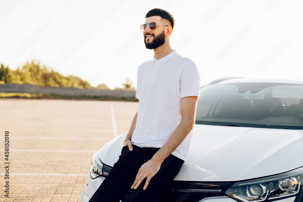 young elegant man, in sunglasses and with a beard, with a luxury car, happy man near the car outdoors young elegant man, in sunglasses and with a beard, with a luxury car, happy man near the car outdoors