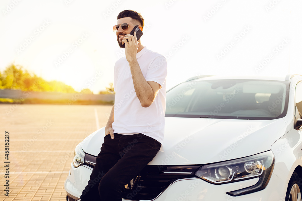 young business man talking on a mobile phone in the city near a white car young business man talking on a mobile phone in the city near a white car