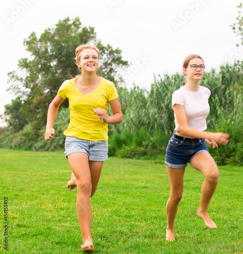 Fototapeta Naklejka Na Ścianę i Meble -  Two young barefoot girls in shorts running on meadow together.