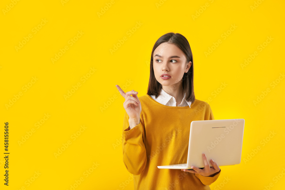 Beautiful young woman with laptop pointing at something on yellow background Beautiful young woman with laptop pointing at something on yellow background