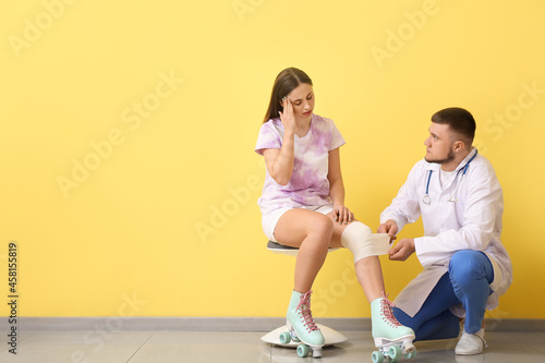 Doctor applying bandage onto knee of young woman near color wall