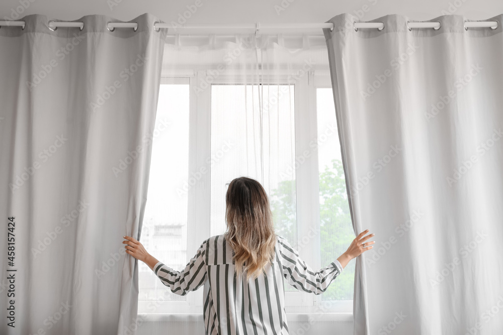 Woman opening light curtains in morning at home Woman opening light curtains in morning at home