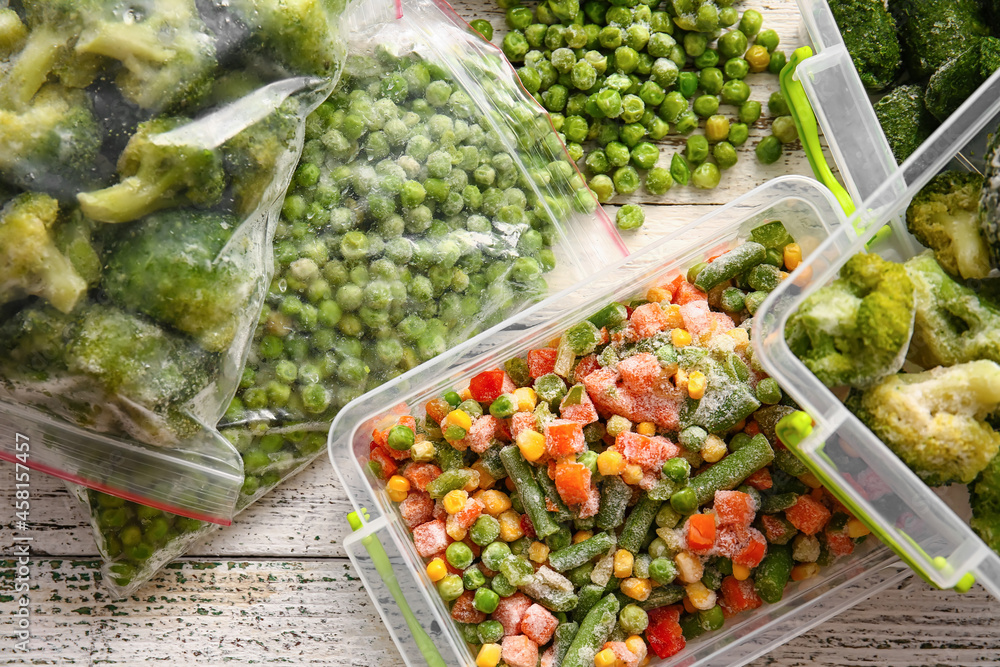 Plastic bags and containers with different frozen vegetables on light wooden background
