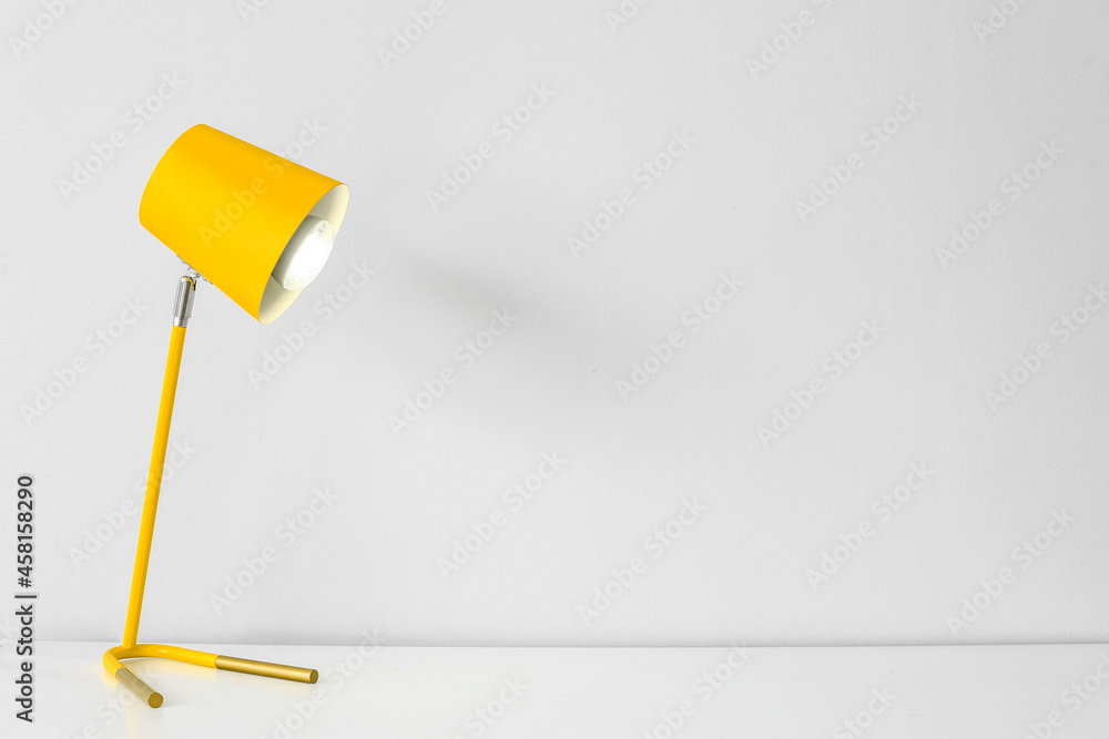Modern glowing lamp on table near white wall Modern glowing lamp on table near white wall
