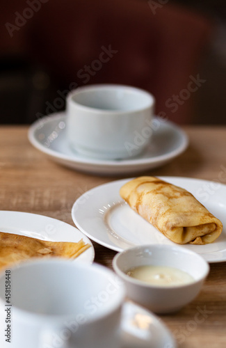 Fresh pancakes with filling on the table next to white mugs for coffee or tea for breakfast. Pancakes for a sweet dessert after lunch in a cozy coffee.