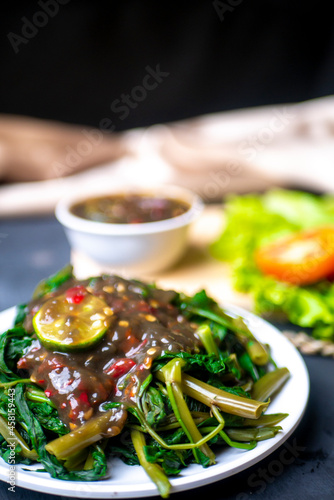 Petis kangkung with lemon, Indonesian Tradional Food from Semarang City on white plate and black background