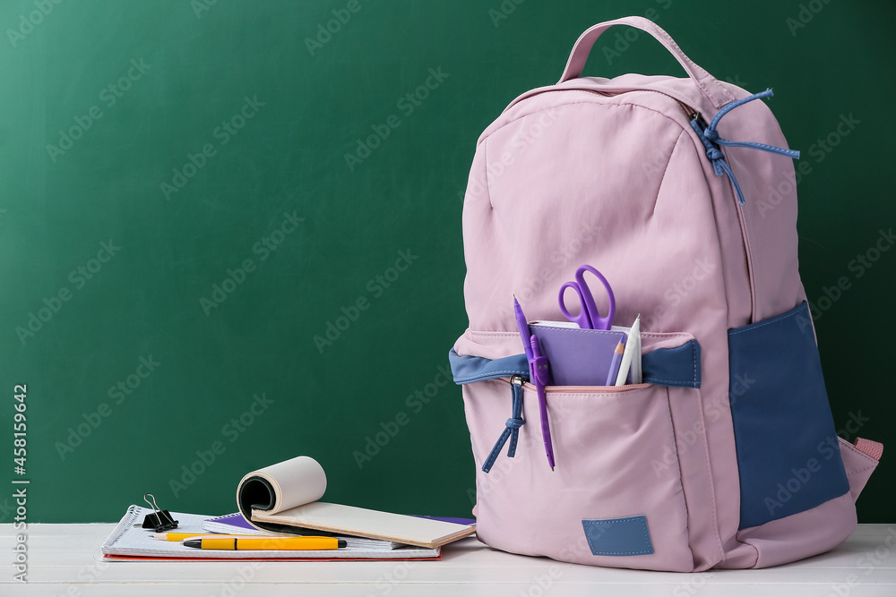 Stylish school backpack with stationery on table against blackboard Stylish school backpack with stationery on table against blackboard