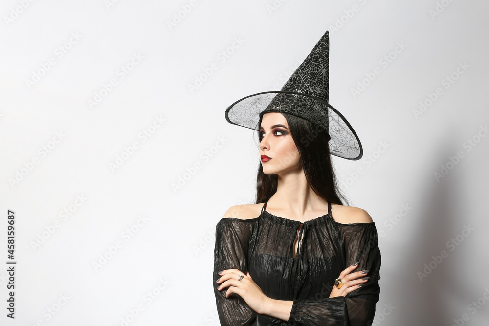 Beautiful woman dressed as witch for Halloween party on light background Beautiful woman dressed as witch for Halloween party on light background