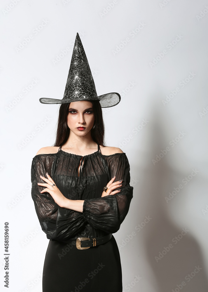 Beautiful woman dressed as witch for Halloween party on light background Beautiful woman dressed as witch for Halloween party on light background