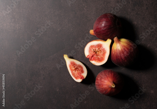 Lots of figs and cut figs on a plate set against a dark background.