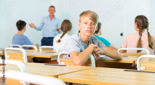 Teenager boy sitting in class room. He have turned around and watching in camera.