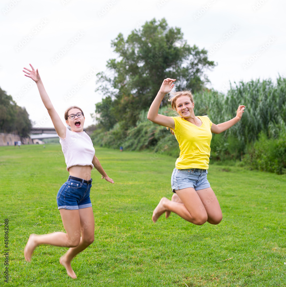 Obraz premium Portrait of cheerful teenage girls jumping together in summer city park. Concept of happy adolescence
