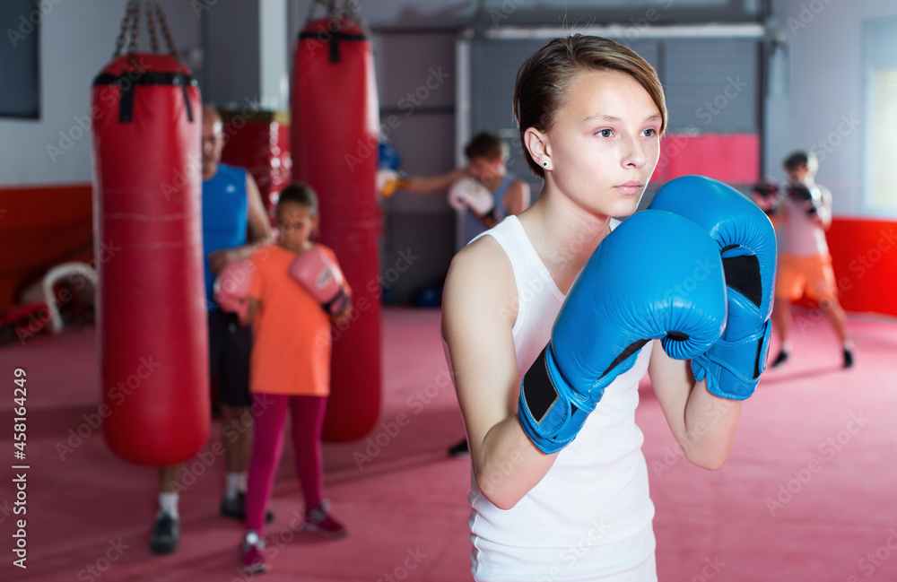 Young serious teenager with boxing gloves posing in defended stance at gym