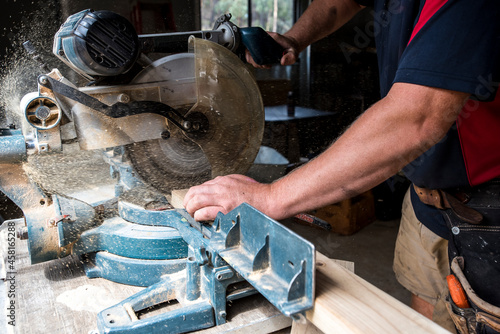 Man cutting timber with drop saw with sawdust coming out of saw