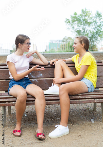 Best friends chatting while sitting on bench in summer park