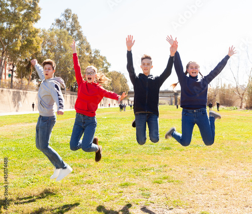 Group of teenagers having fun together outdoors, jumping on green lawn in springtime