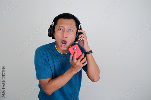 Asian young man wearing headphones and holding a smartphone with singing gesture isolated on white background. photo