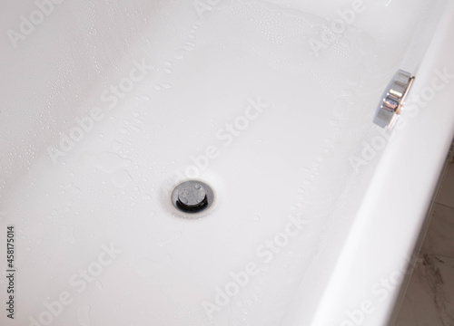 Modern silver drain plug in a new bathroom, water droplets on the walls of the bathtub. Copy space for text