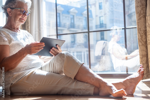 Free Download Senior traveler woman in hotel room sitting on the floor consulting her digital tablet to organize a city tour - GFXLoad
