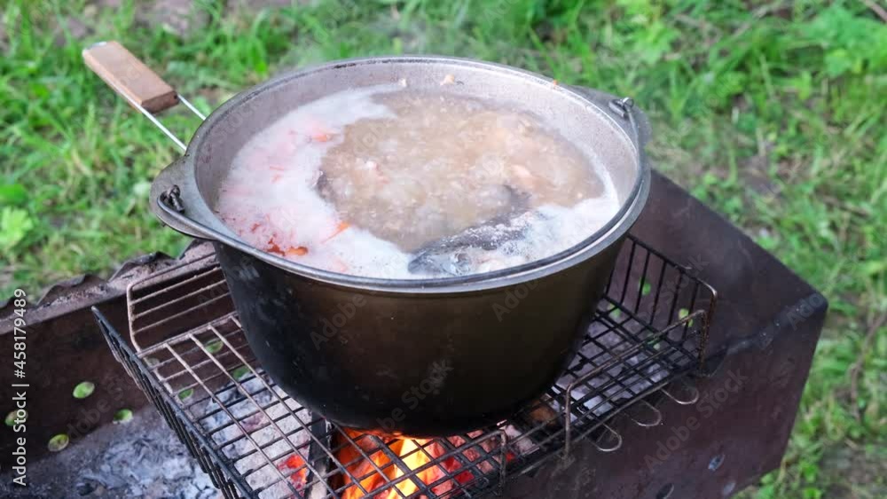 Boil fish soup in a pot over the fire. Hike in nature. The concept of outdoor activities, camping, picnic, fishing, cooking, travel and tourism, vacation Boil fish soup in a pot over the fire. Hike in nature. The concept of outdoor activities, camping, picnic, fishing, cooking, travel and tourism, vacation