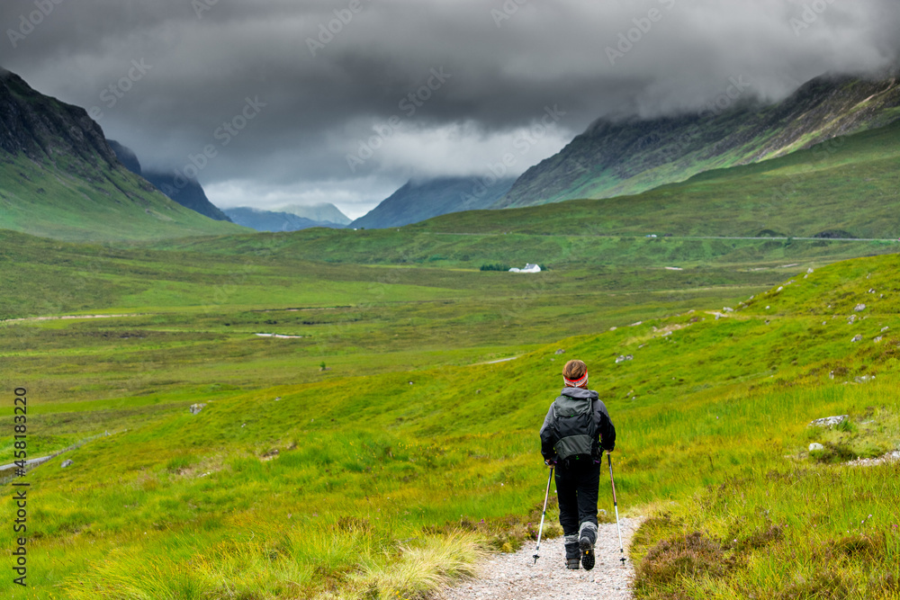 Along the West Highland Way. A lonely hiker walks on the hiking path in the green valley of Glen Coe.