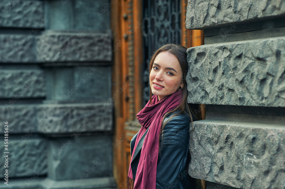Naklejka premium A stylish young girl in a fashionable leather jacket on a city street .