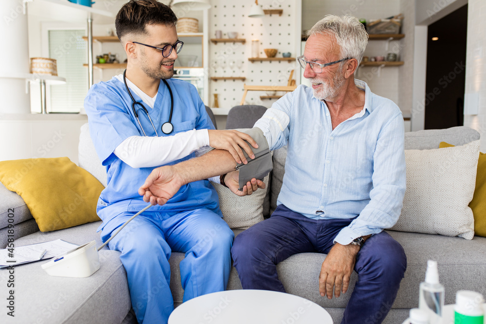Fototapeta premium Male nurse measures blood pressure to senior man with mask while being in a home visit.
