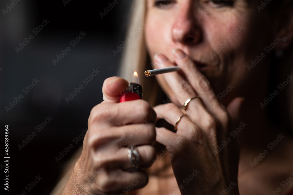 Obraz premium Mid-aged woman lighting a cigarette at home, getting her nicotine daily dose, unable to resist to her unhealthy habit