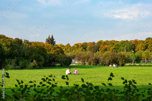 A couple of young people are sitting on the green grass on great lawn grass meadow in autumn fall season photo