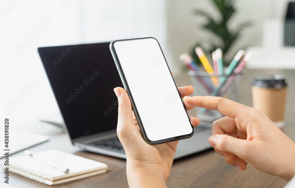 Close up of hand holding smartphone with white mock-up screen in office Close up of hand holding smartphone with white mock-up screen in office
