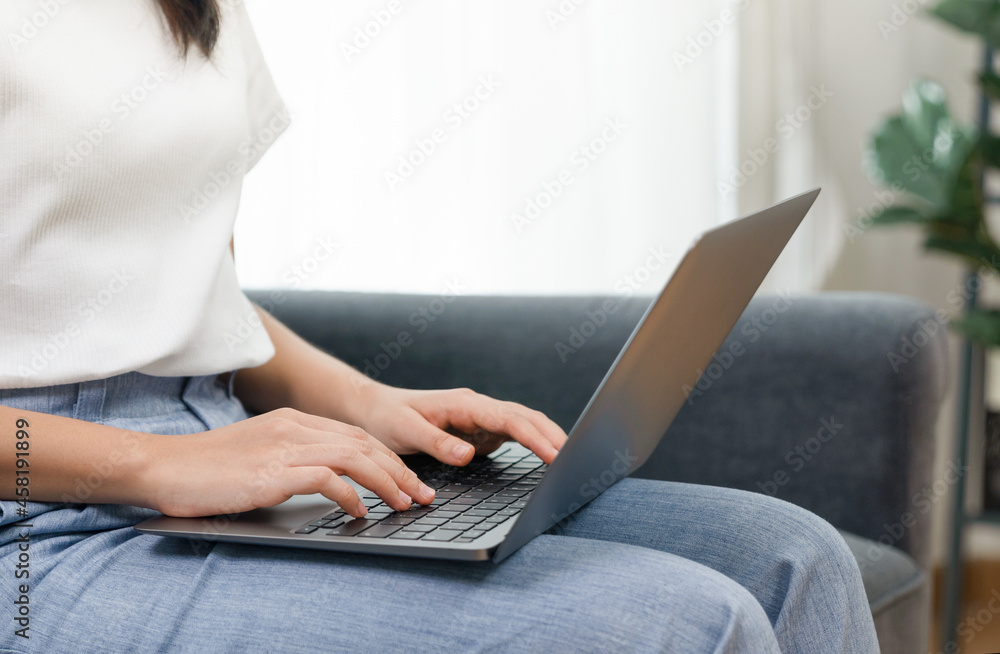 Fototapeta premium Woman using laptop sitting on sofa in living room.