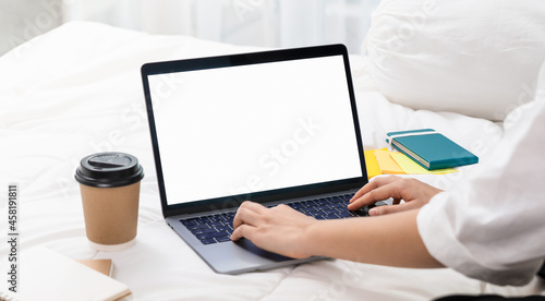 Woman using and typing on Laptop with a mockup white screen on bed.
