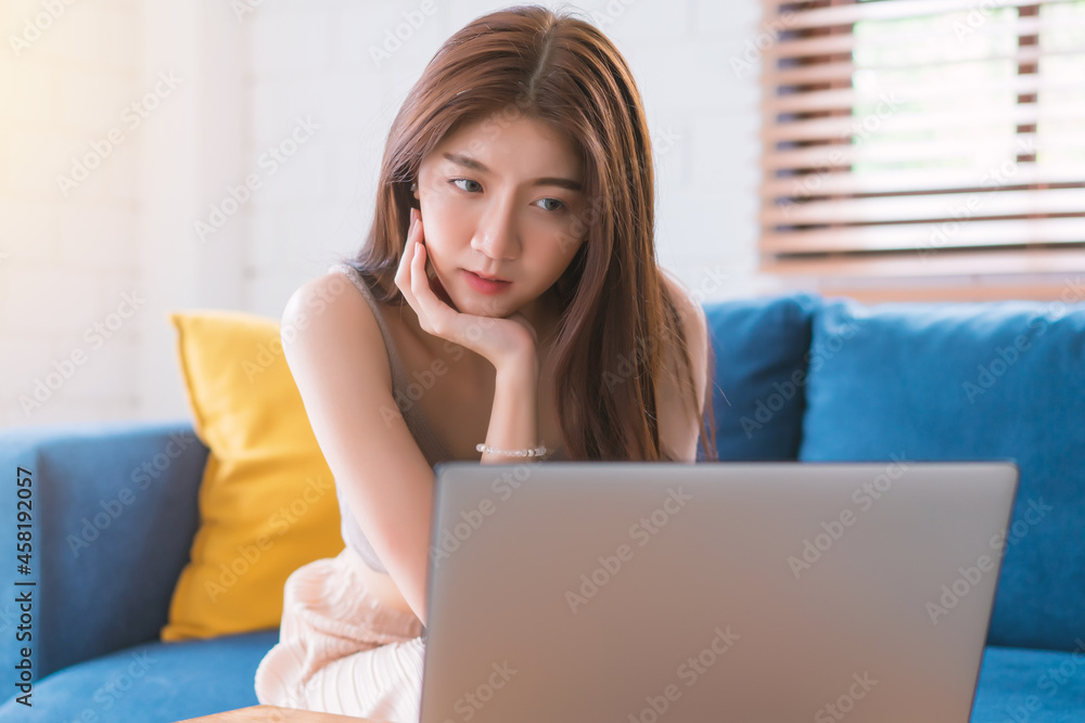 Asian woman relaxing sitting on sofa using computer notbeook at living room, Education technology and internet concept Asian woman relaxing sitting on sofa using computer notbeook at living room, Education technology and internet concept