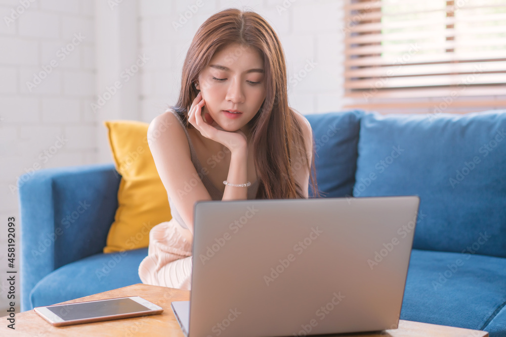 Asian woman relaxing sitting on sofa using computer notbeook at living room, Education technology and internet concept Asian woman relaxing sitting on sofa using computer notbeook at living room, Education technology and internet concept