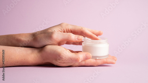 Womans hands holding cosmetic cream container on violet. Hand holding cream jar on purple