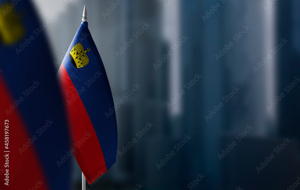 Small flags of Liechtenstein on a blurry background of the city - obrazy, fototapety, plakaty 