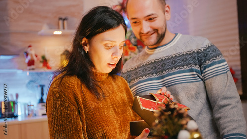 Woman receiving present from man on christmas day. Man giving gift box with ribbon and bow tie to partner, feeling cheerful about holiday season. Couple celebrating winter festivity