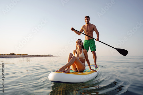 Photography Couple of tourists young man and woman having fun paddleboarding at sea
