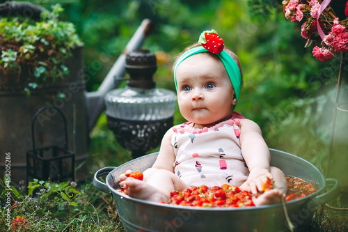 A little girl bathes in a basin with strawberries in the garden.