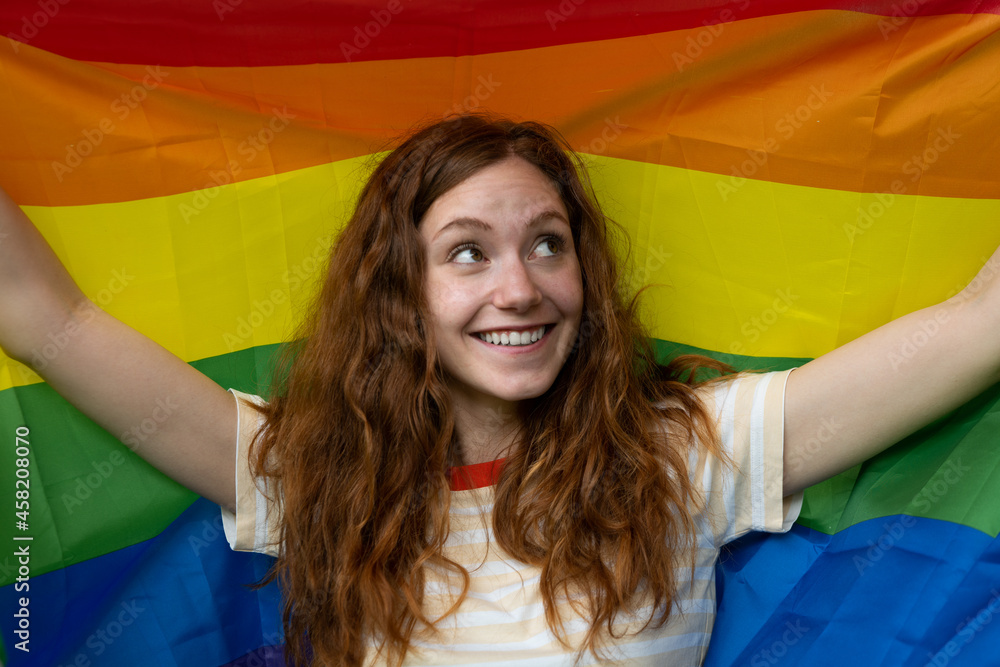 © Kitreel - Cinematic shot of happy young red hair woman carrying flag of LGBT rainbow symbol and smiling in camera in green city park. Concept of homophobia, diversity, equity, peace and love, freedom, liberty. © Kitreel - Cinematic shot of happy young red hair woman carrying flag of LGBT rainbow symbol and smiling in camera in green city park. Concept of homophobia, diversity, equity, peace and love, freedom, liberty.