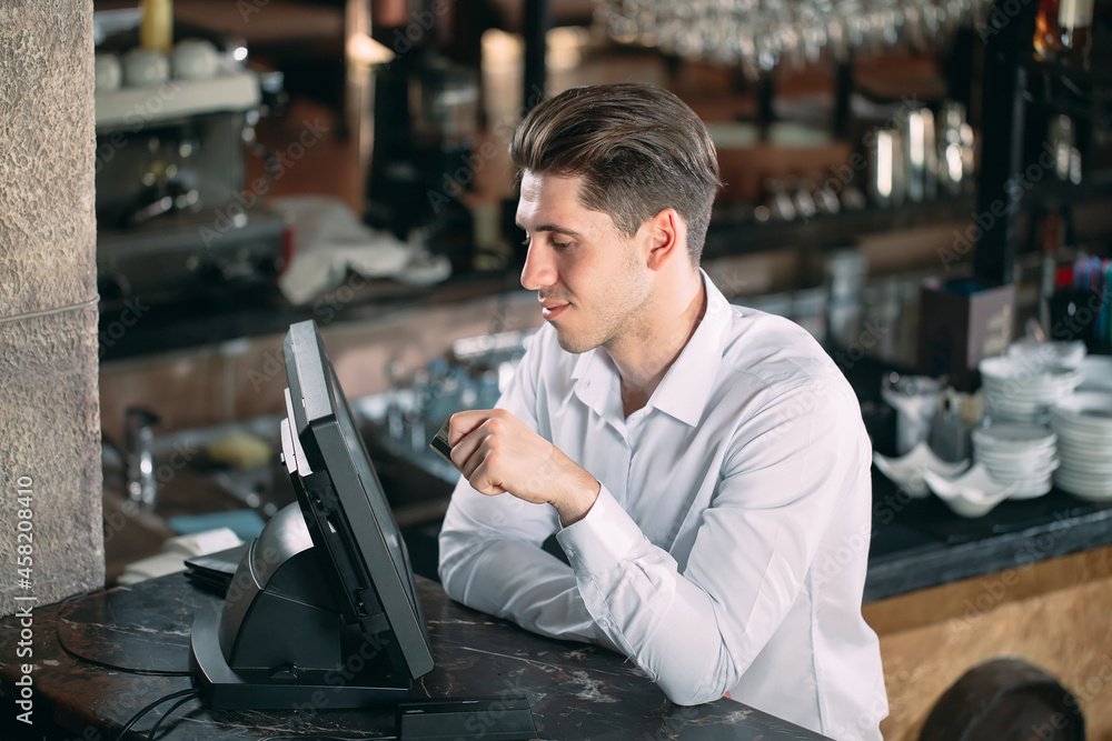 small business, people and service concept - happy man or waiter in apron at counter with cashbox working at bar or coffee shop. small business, people and service concept - happy man or waiter in apron at counter with cashbox working at bar or coffee shop.